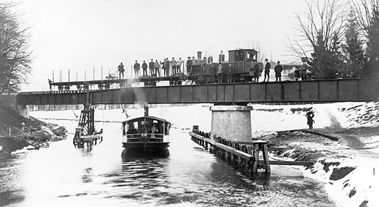 Den svngbara jrnvgsbron ver Gta kanal har just blivit frdigstlld. ret r 1914 och p bron syns ett byggnadstg draget av lok MJ nummer 5. Till vnster i bild ligger stationen i Motala.