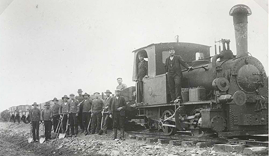 WbÄJ byggnad. Entreprenören Saabye & Lerche's anläggningslok Hanomag 4573 1906 B. Gruståg med rallare uppställda framför vagnarna.