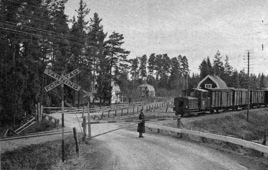 SJ- Rationaliseringen yttrar sig, också genom nedläggandet av bl. a. trafiksvaga bandelar. I farozonen sedan några år är den lilla smalspårsjärnvägen Eksjö - Österbymo, där i första hand person- och styckegodstrafiken är hotad. Här kommer lokomotortåget förbi vägövergången i Perstorp, bevakad av vägvakten Hanna Jonansson. 1 personvagn, 3 godsfinkor